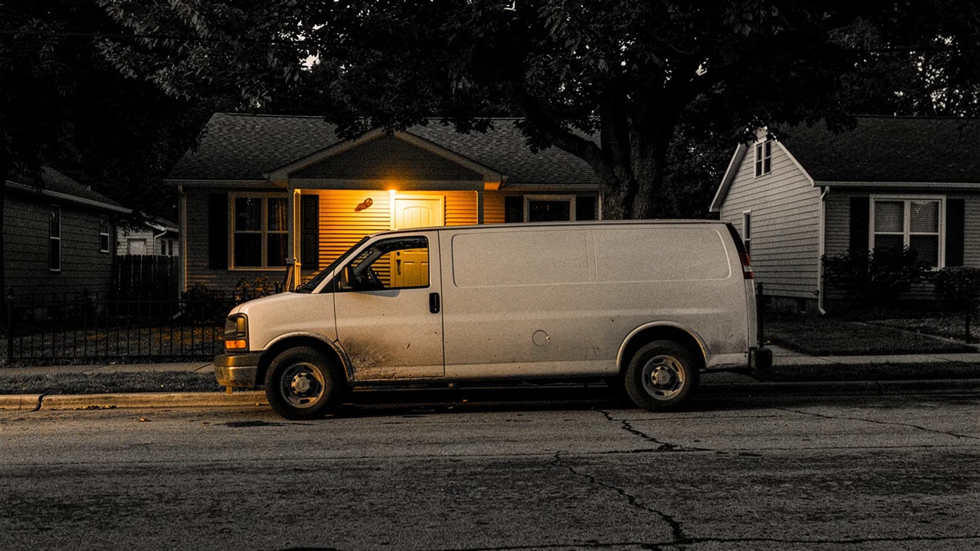 Work van parked at the curb at dusk in front of a small house with its porch light on
