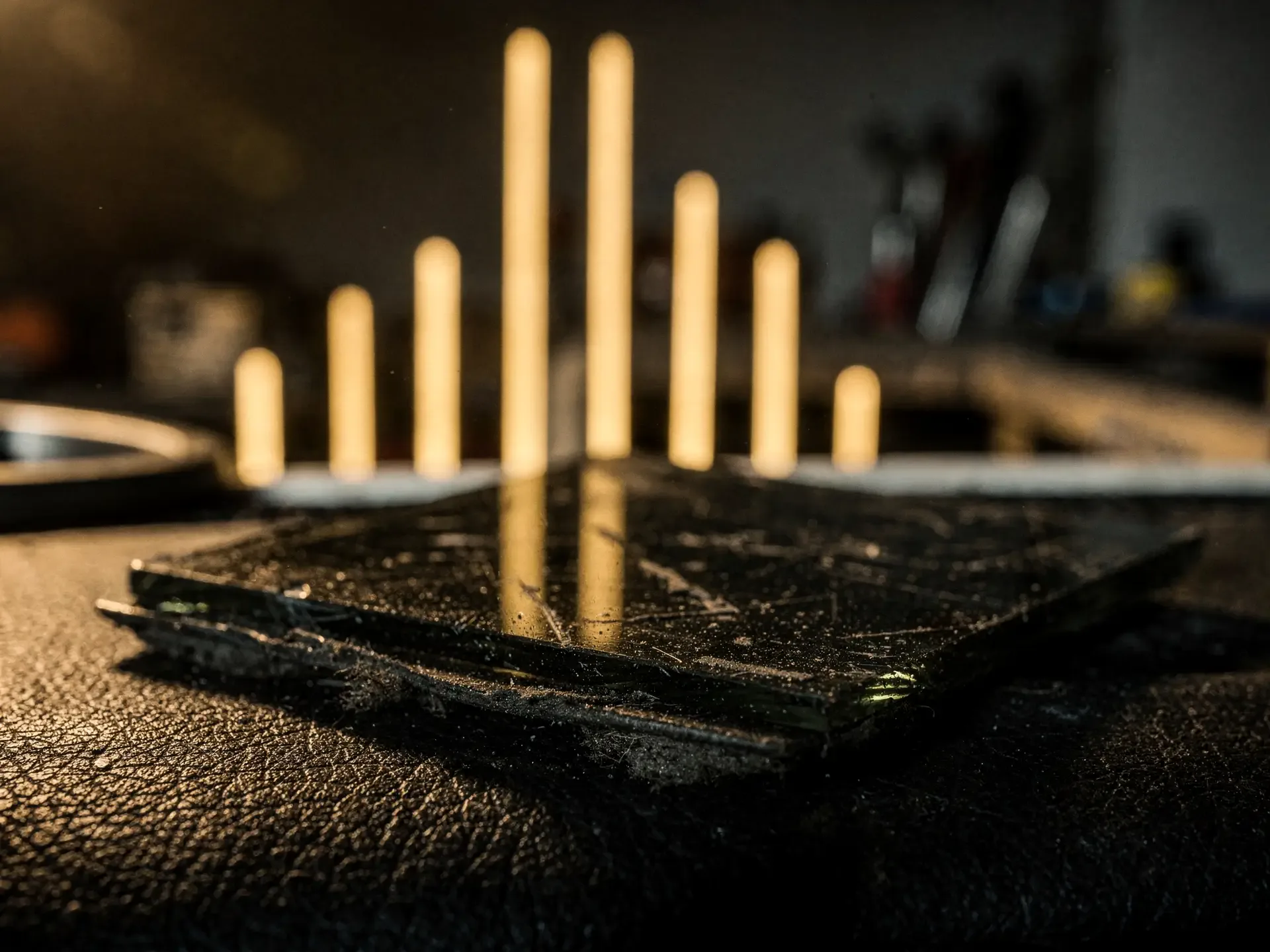 Seven soft gold bars of light rising behind a scratched dark glass tile on black leather