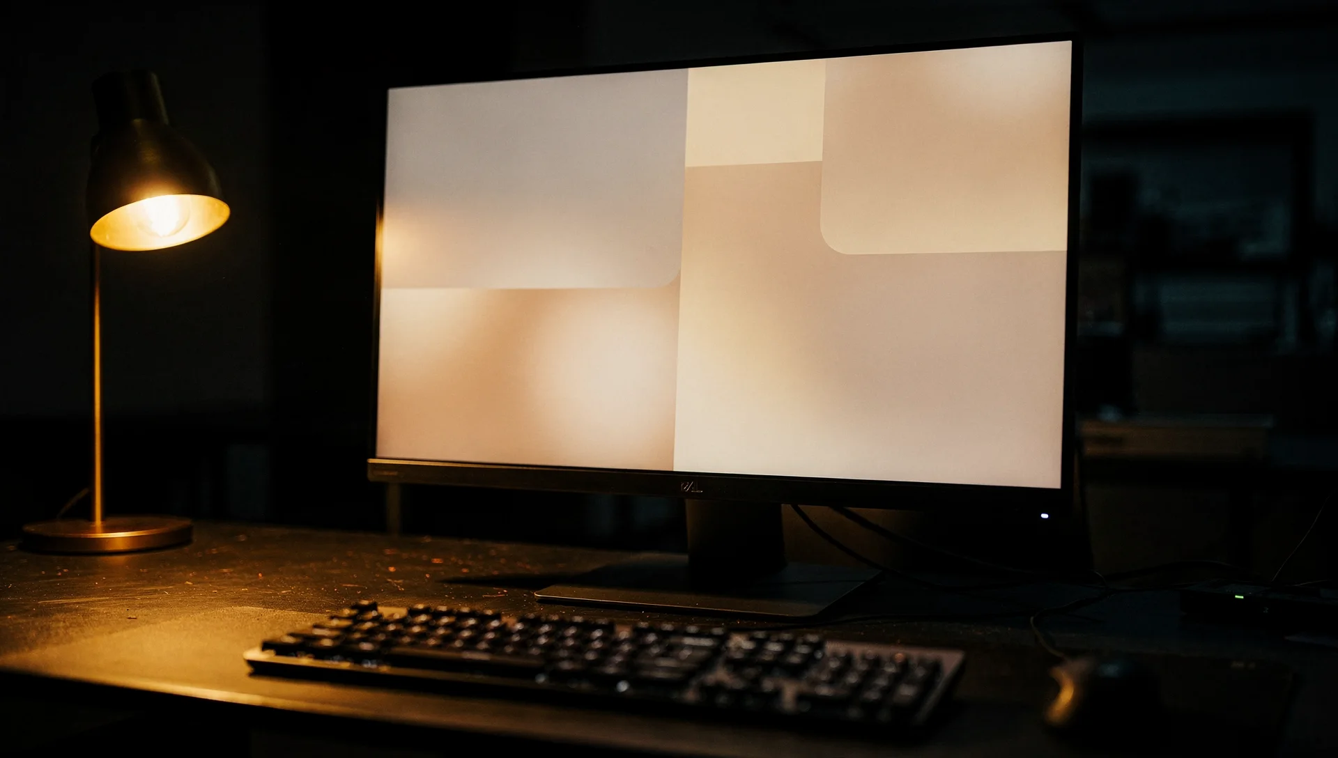 A monitor showing soft abstract layout blocks beside a brass lamp on a dark studio desk